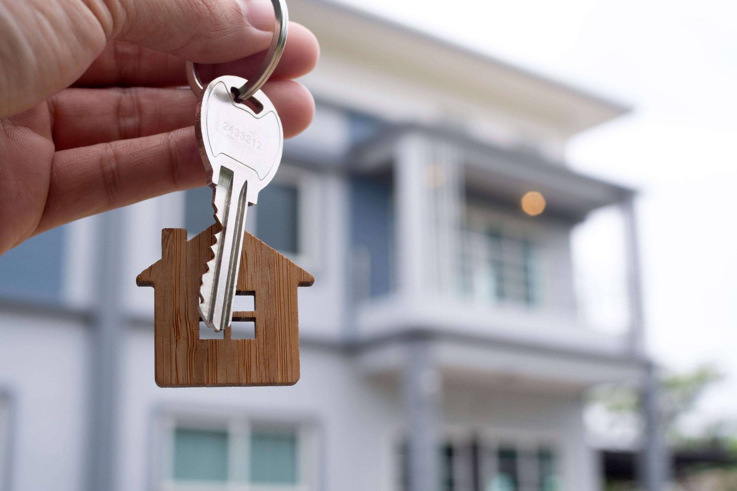 Comprar una casa por primera vez - mano sosteniendo las llaves frente a una casa